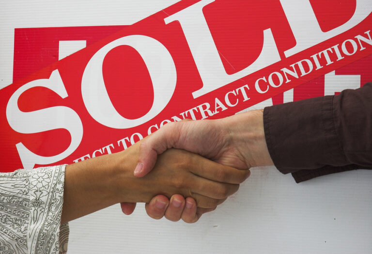 people shaking hands in front of a commercial property business sold sign